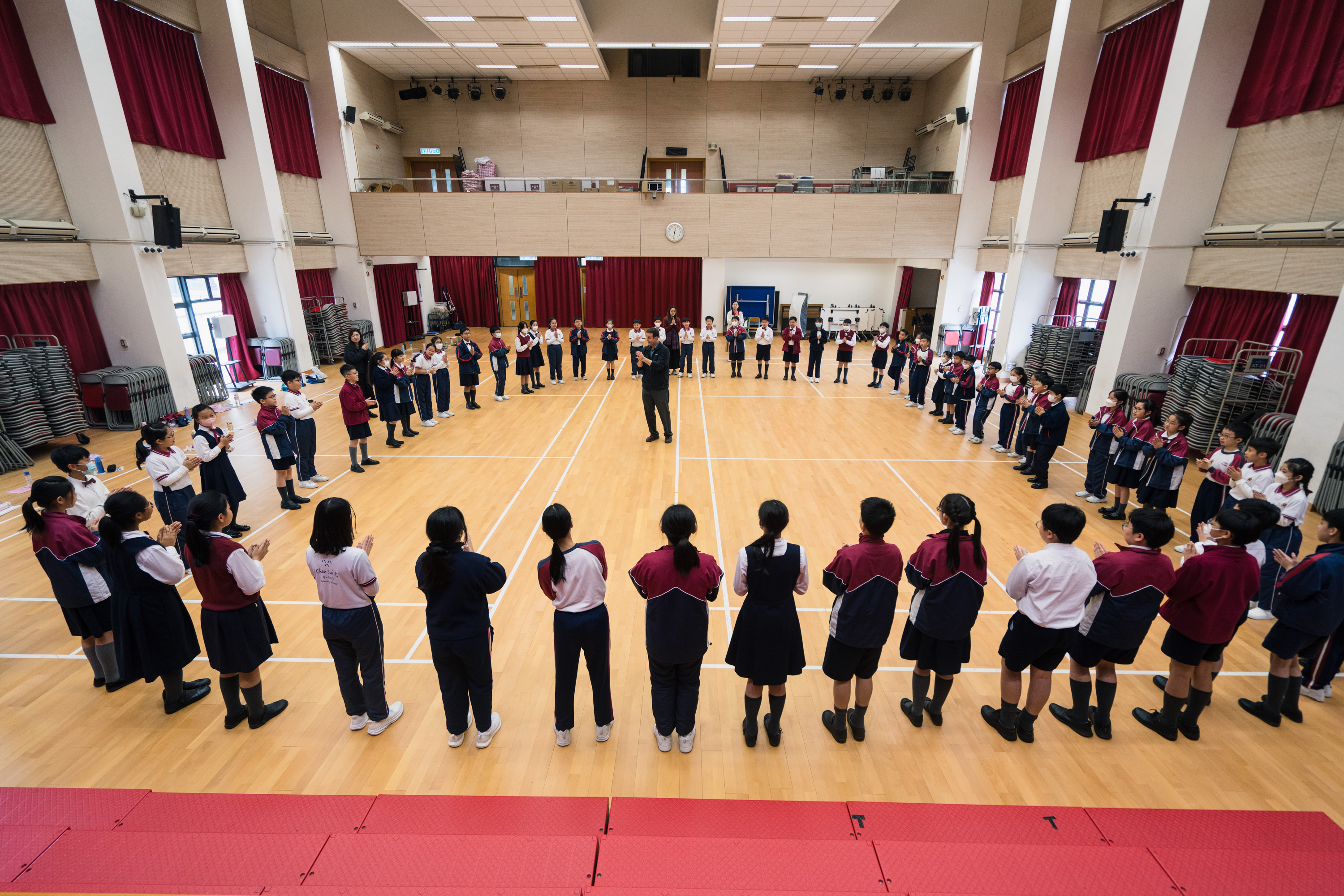 Students standing in a large circle around a conductor in a school hall during an HKVC choral workshop